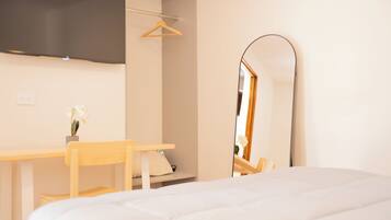 A bedroom with a bed, a desk, a chair, a TV mounted on the wall, and a mirror.