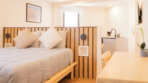 Quarto com cama, cabeceira de madeira, mesa de cabeceira, escrivaninha e cadeira.