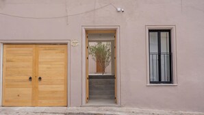 Um edifício com uma porta dupla de madeira, uma pequena janela com grade de metal e uma escadaria que leva a uma porta com uma placa em cima.
