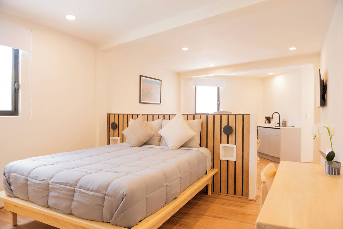 Un dormitorio con cama, mesita de noche y una pequeña zona de escritorio.