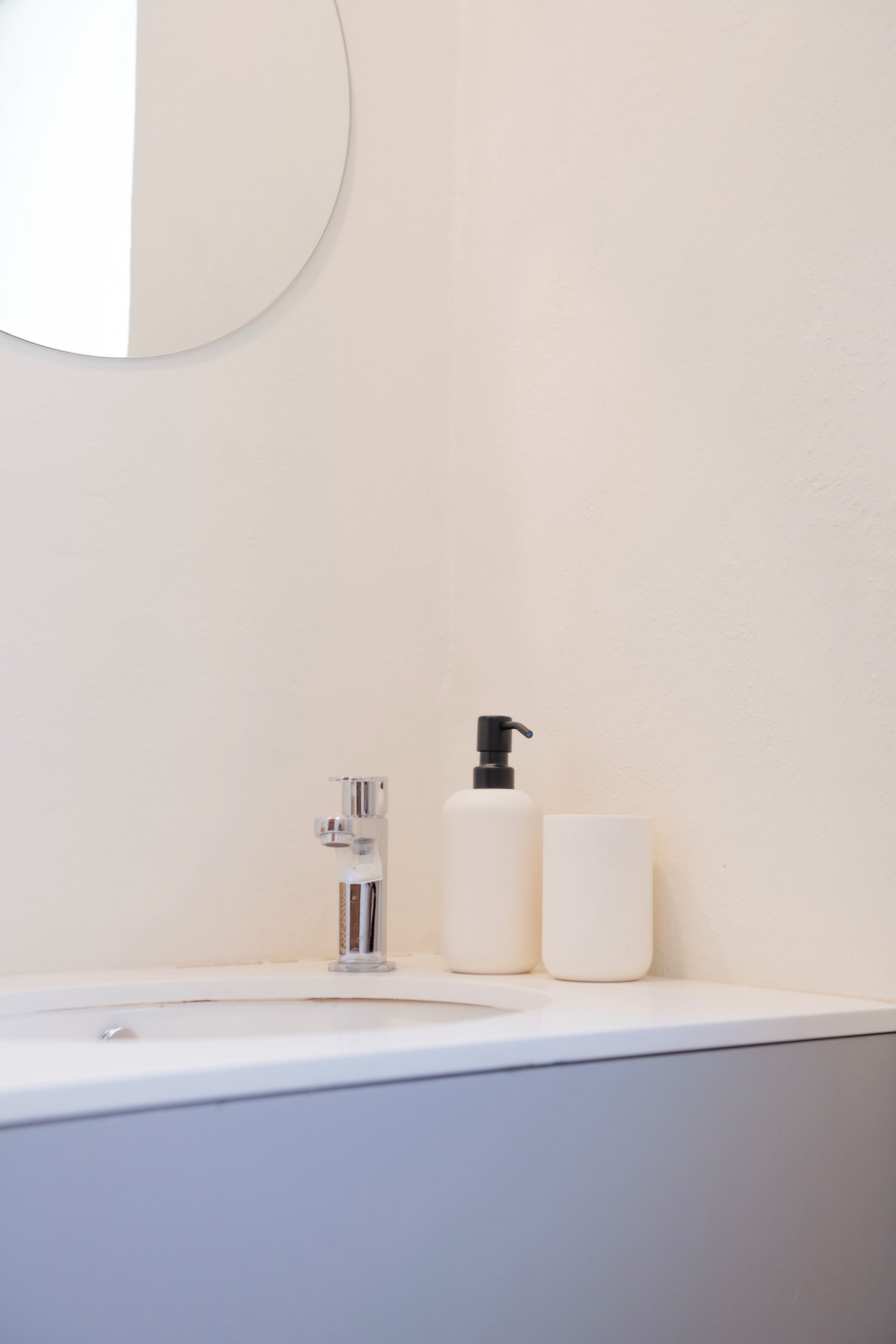 A bathroom with a white sink, a mirror, and two white bottles on the counter.