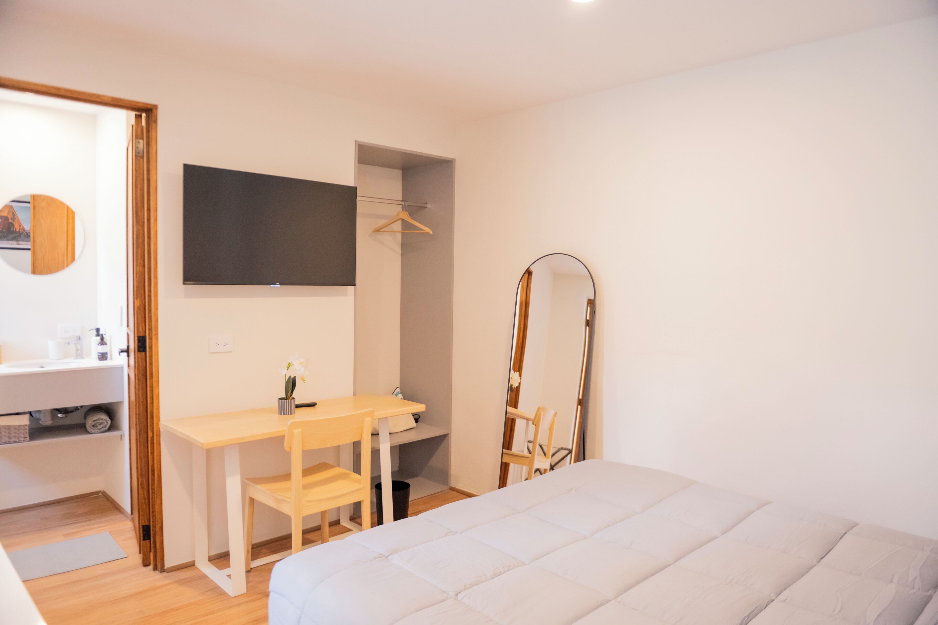A bedroom with a bed, a desk, a chair, a mirror, and a wardrobe.