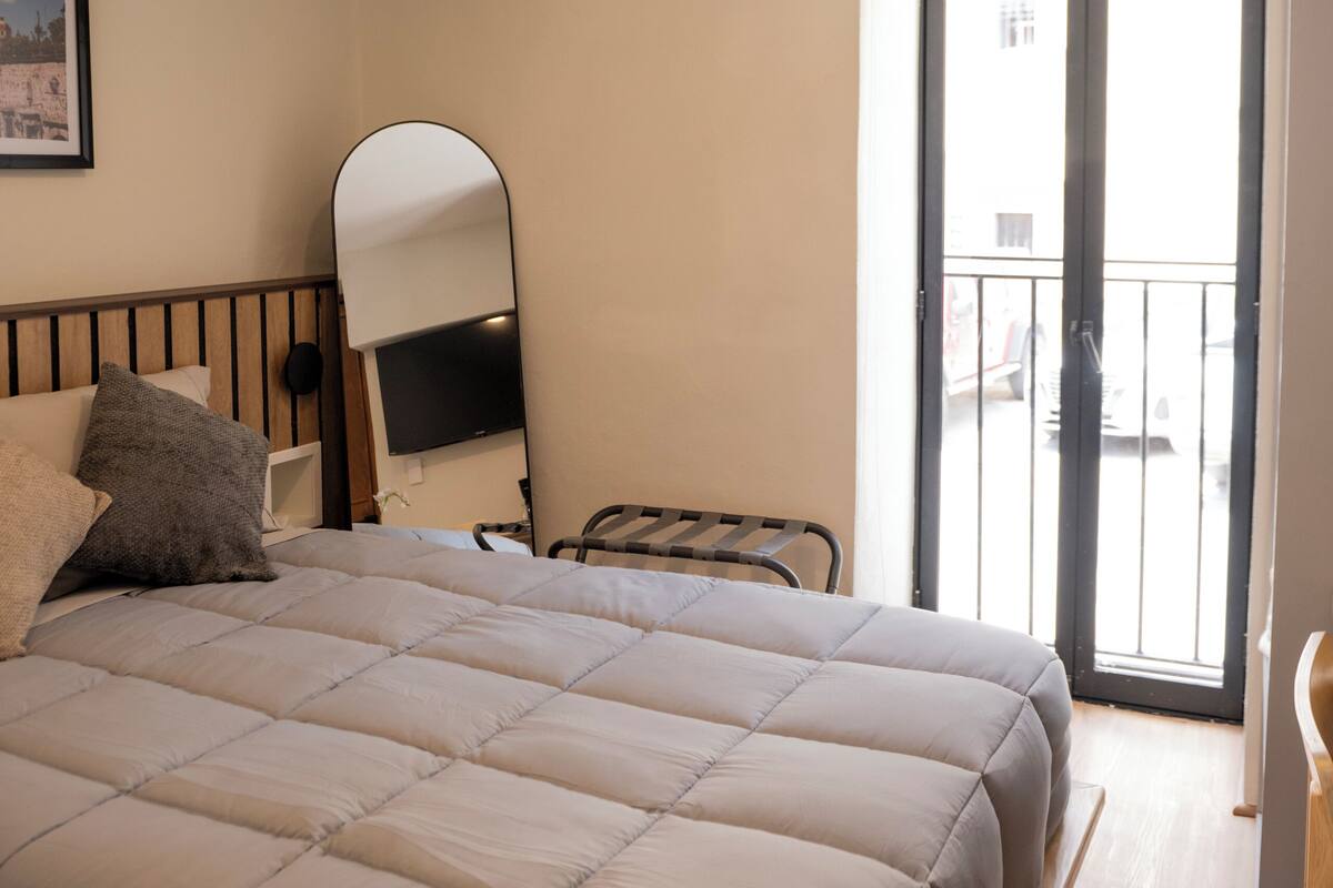 Un dormitorio con cama, espejo, puerta que da a un balcón y un cuadro en la pared.