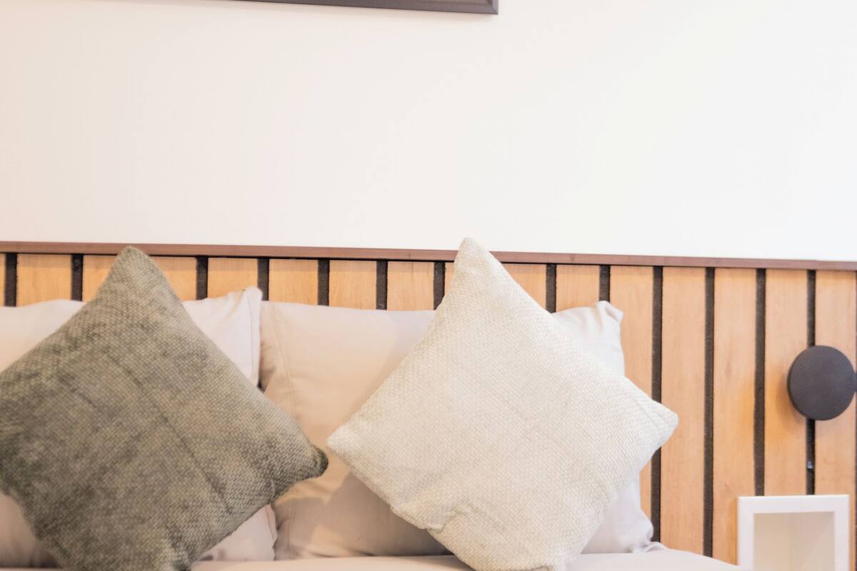 Una cama con cabecera, almohadas y un cuadro en la pared.