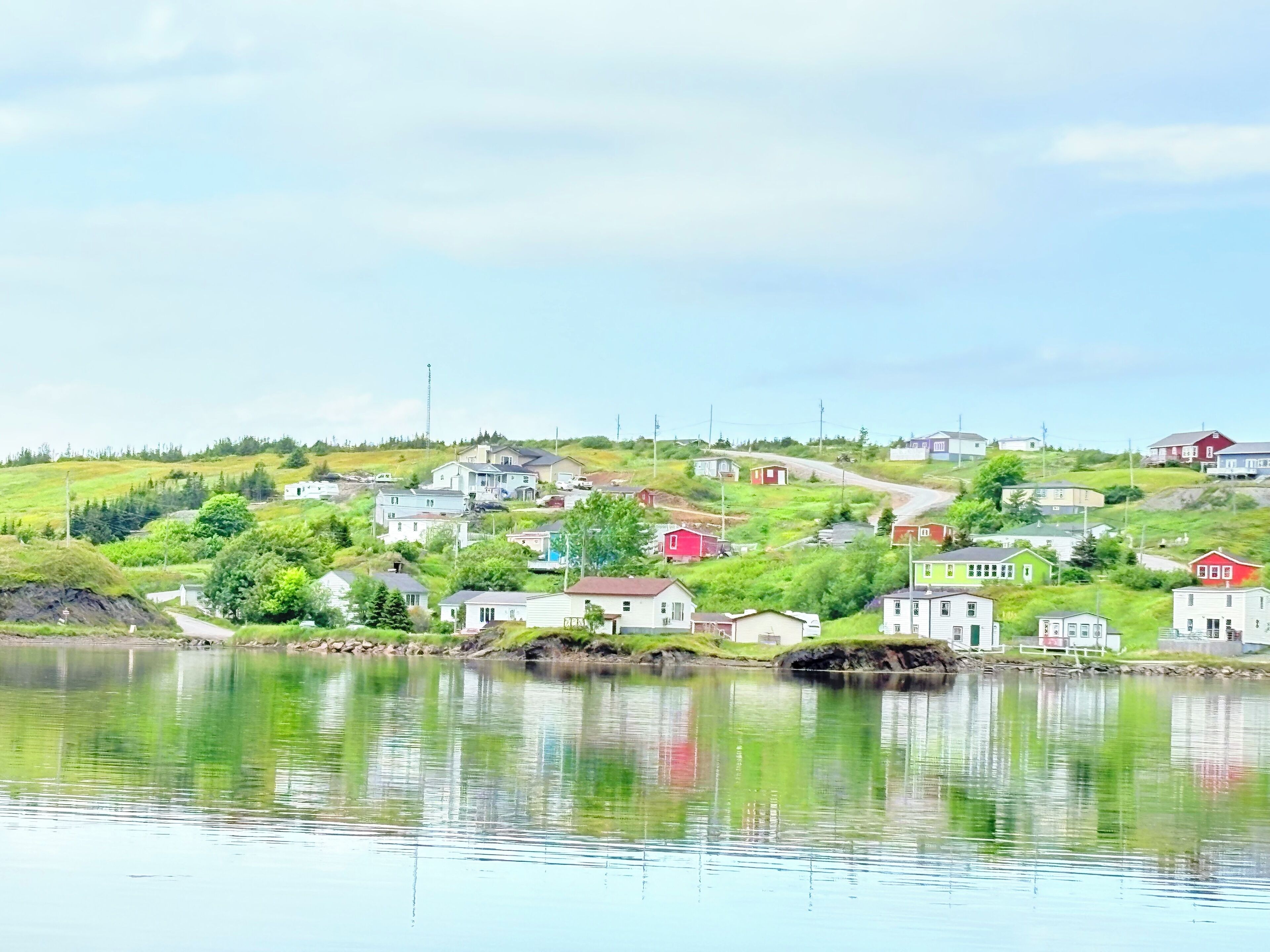 Une vue sur un petit village au bord d’un lac, avec des maisons construites sur une colline, un ciel dégagé et une eau calme qui reflète les bâtiments.