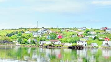 Une vue sur un petit village au bord d’un lac, avec des maisons construites sur une colline, un ciel dégagé et une eau calme qui reflète les bâtiments.