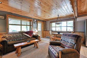 Ein gemütliches Blockhaus-Interieur mit Sofa, Sessel, Holztisch und großen Fenstern.