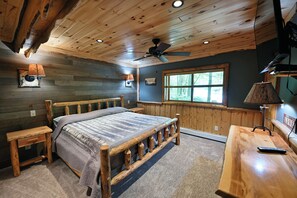 Ein Schlafzimmer in einer Holzhütte mit einem Bett, einem Schreibtisch, einem Deckenventilator und einem Fenster.