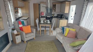 A compact living space with a sofa, armchair, dining table, kitchenette, and a TV. - Seaside Retreat in New Milton, up to 6 Guests (New Milton)