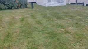 A grassy yard with a white building in the background. - Seaside Retreat in New Milton, up to 6 Guests (New Milton)
