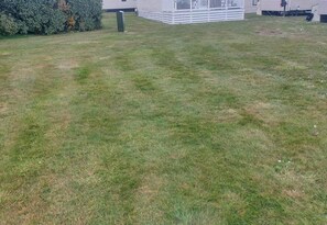 A grassy yard with a white building in the background. - Seaside Retreat in New Milton, up to 6 Guests (New Milton)