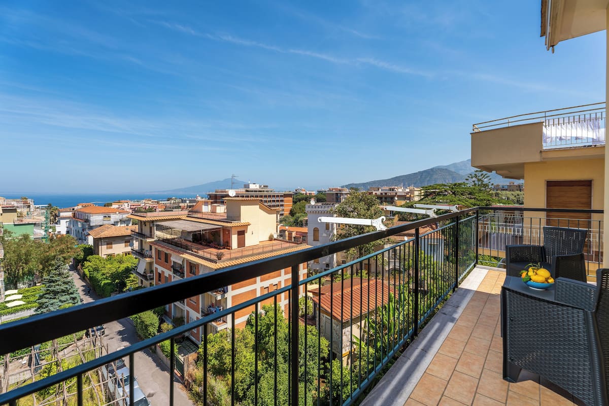 Un balcon offrant une vue sur le paysage urbain, avec des bâtiments et une montagne visible au loin.