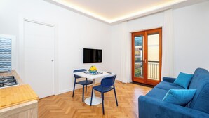 A compact living space with a dining area, a sofa, a TV, and a wooden floor. - YourHome - Nerea & Nicea Apartments (Sorrento)