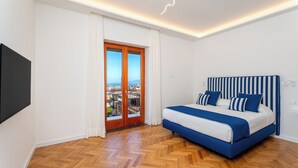A bedroom with a bed, a TV, a view through a door, and a herringbone floor. - YourHome - Nerea & Nicea Apartments (Sorrento)