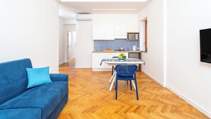 A modern living room with a blue sofa, a dining area with a table and chairs, and a kitchen with white cabinets and a microwave. - YourHome - Nerea & Nicea Apartments (Sorrento)