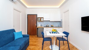 A compact living space with a sofa, dining table, chairs, a kitchen area, and a TV mounted on the wall. - YourHome - Nerea & Nicea Apartments (Sorrento)