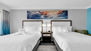 Habitación de hotel con dos camas, una mesita de noche, una obra de arte en la pared y vista al océano.