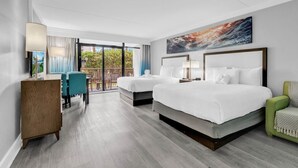 Habitación de hotel con dos camas, un escritorio, una silla y un balcón con vistas.