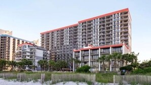 Un hotel moderno de gran altura con varios balcones, techo rojo y vistas a la playa.
