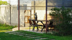 A covered outdoor patio with a grill, metal chairs, and a table. - Dolon Hostel (Bishkek)