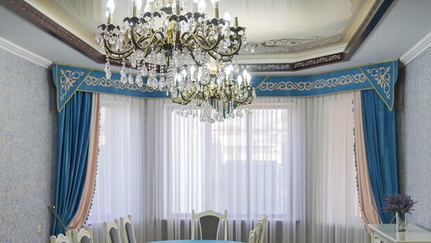 A room with a chandelier, a dining table, chairs, a window with curtains, and a cabinet. - Dolon Hostel (Bishkek)