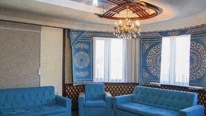 A room with a chandelier, two blue sofas, patterned walls, and a patterned rug. - Dolon Hostel (Bishkek)