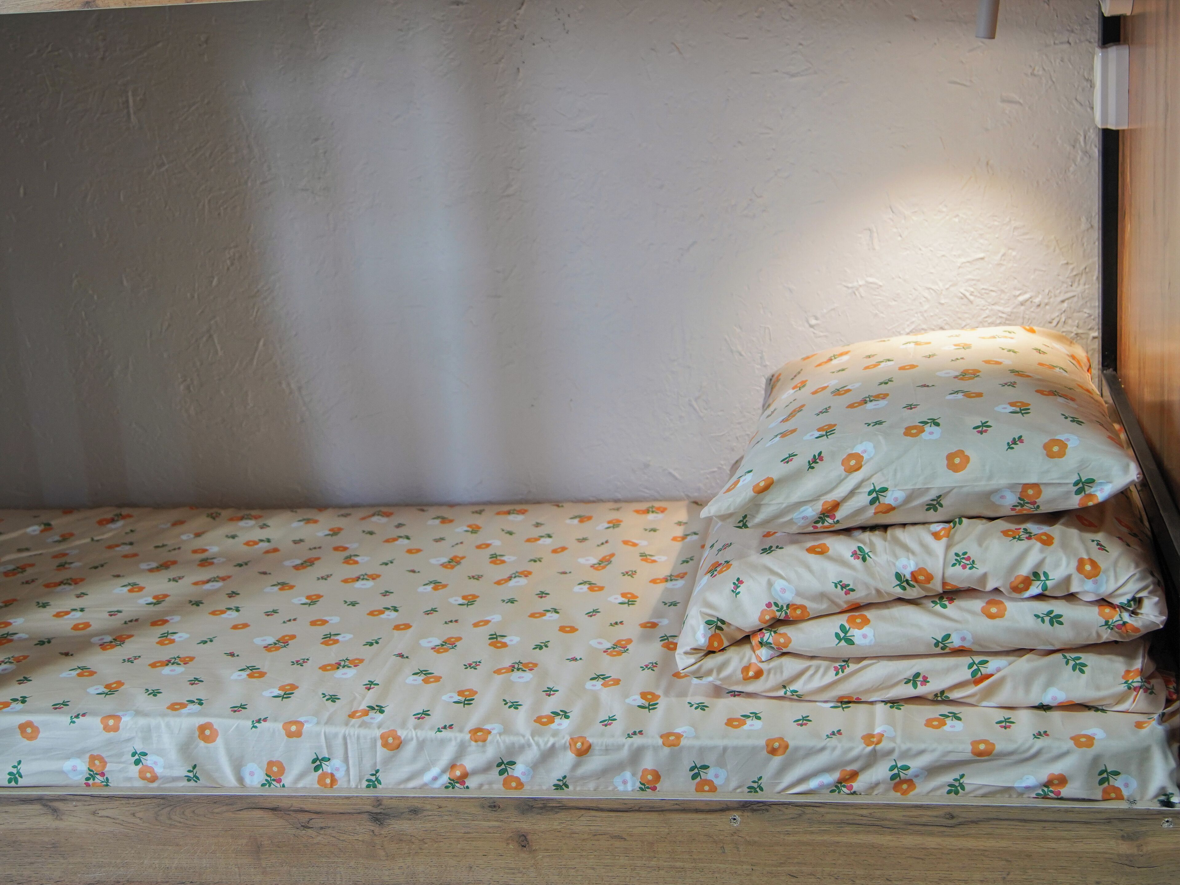 A single bed with a floral-patterned bedspread and pillows, a wooden headboard, and a textured wall.