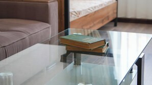 A glass-top table with a book, a brown sofa, and a bed with patterned pillows in a room with wooden paneling. - Dolon Hostel (Bishkek)