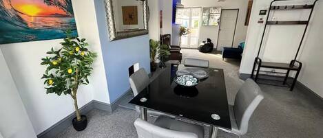 A dining area with a table, chairs, a potted plant, and a painting on the wall.