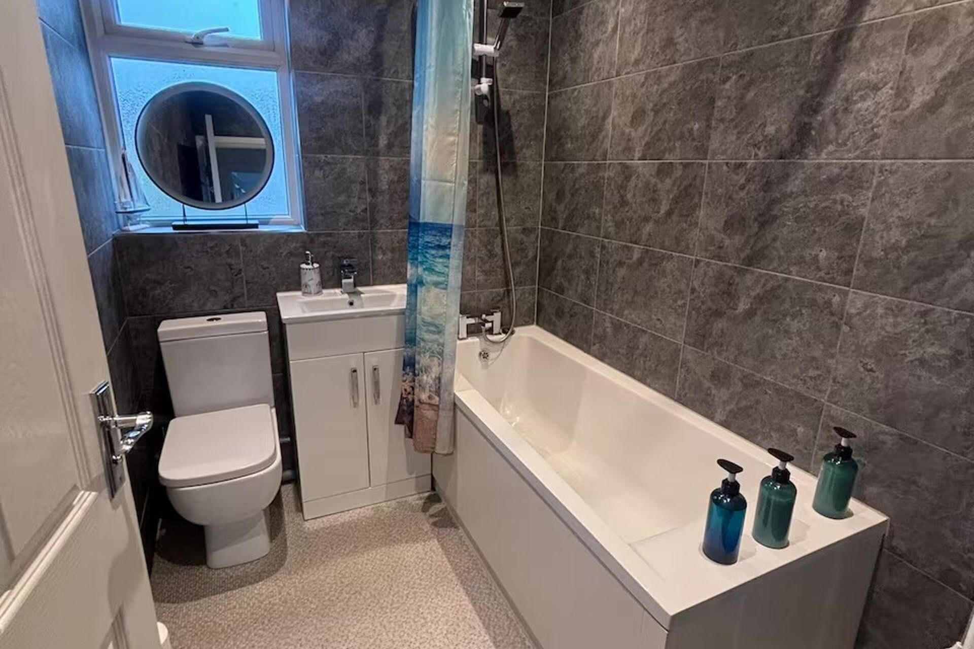 A bathroom with a toilet, sink, bathtub, and three soap dispensers.