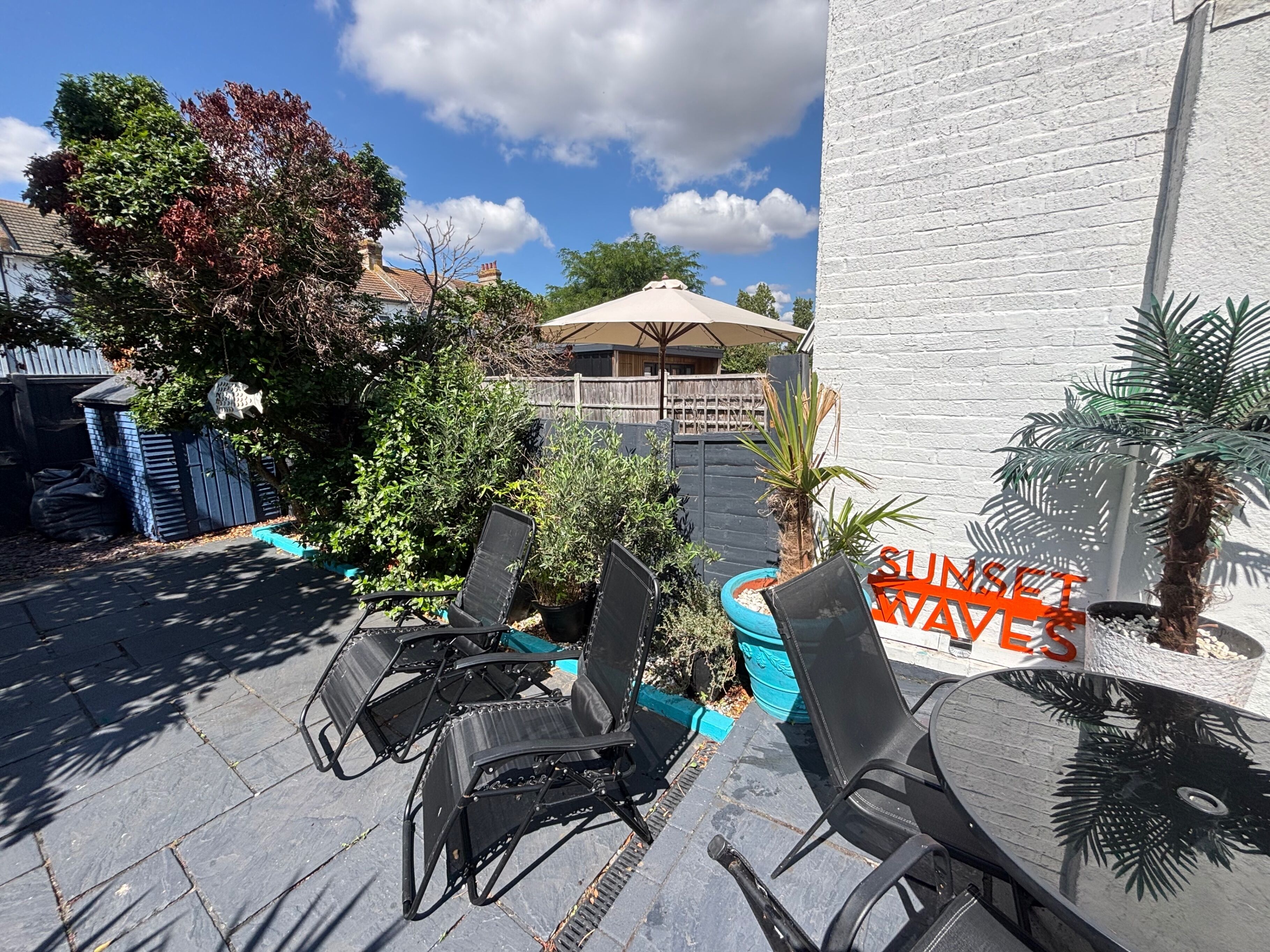 A patio area with outdoor seating, a sign reading 'SUNSET WAVES,' and a white building in the background.