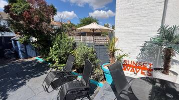 A patio area with outdoor seating, a sign reading 'SUNSET WAVES,' and a white building in the background.