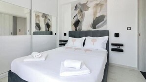 Una habitación de hotel moderna con una cama grande, un espejo, arte abstracto en la pared y una mesita de noche con una lámpara.