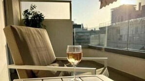 Un balcón con una mesa, una silla, una copa de vino y un libro abierto.