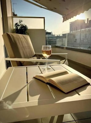 Ein Balkon mit Tisch, Stuhl, einem Weinglas und einem offenen Buch.