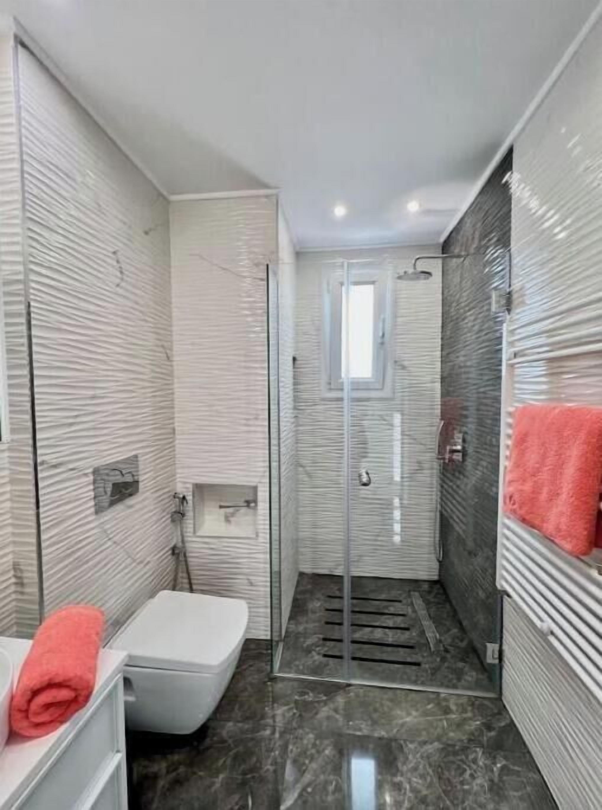 A modern bathroom with a shower, toilet, and a towel rack.
