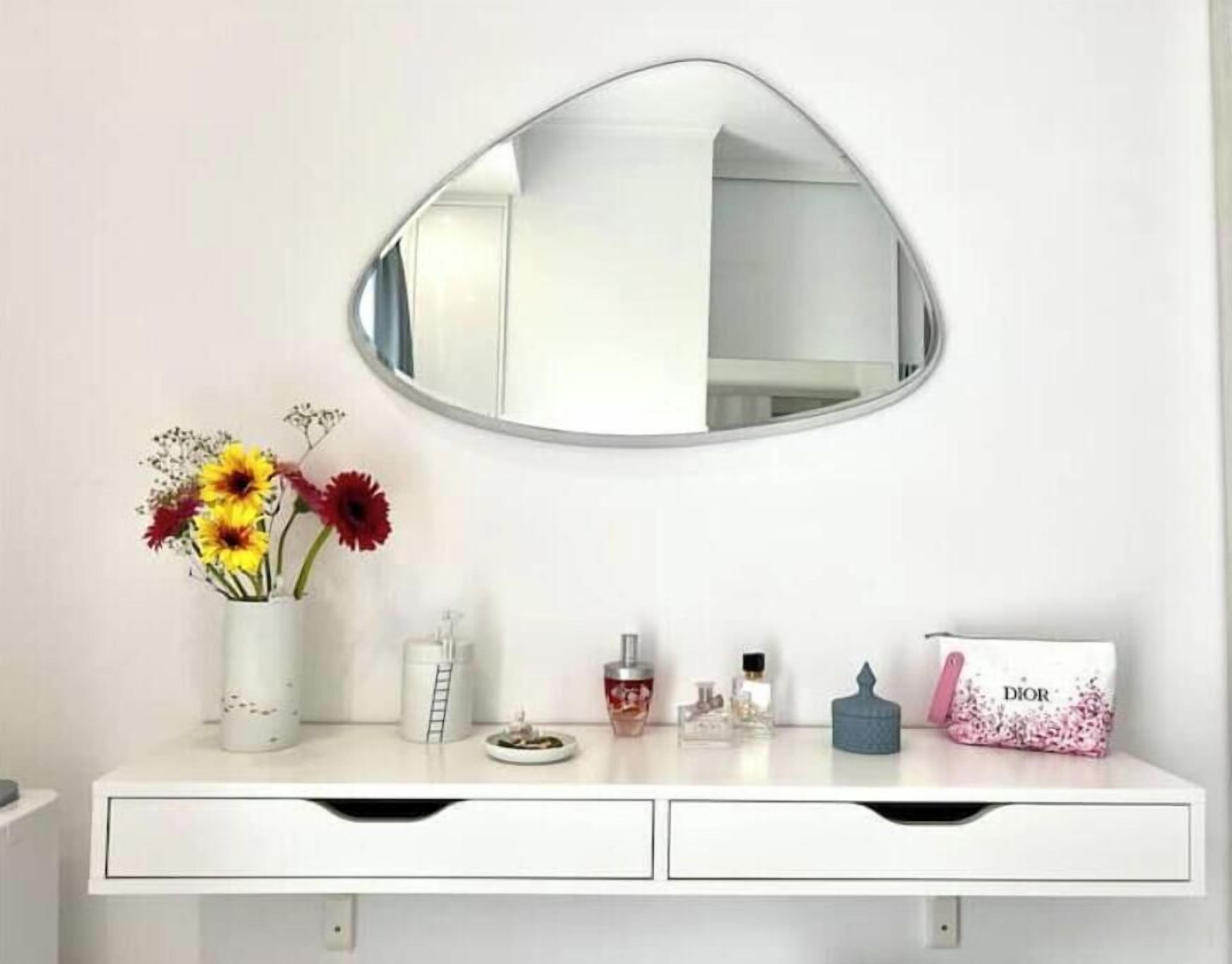 A bathroom vanity with a mirror, a vase with flowers, and a Dior perfume box.