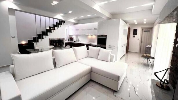 Una sala de estar moderna con un sofá seccional blanco, una cocina al fondo y una escalera.