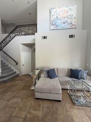Ein Wohnzimmer mit einem Ecksofa, einem Glastisch und einer Treppe mit aufwendiger Geländerarbeiten.