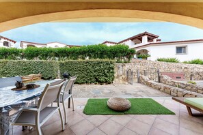 Eine Terrasse im Freien mit Esstisch und Stühlen, einem runden gewebten Pouf und einer Steinmauer.
