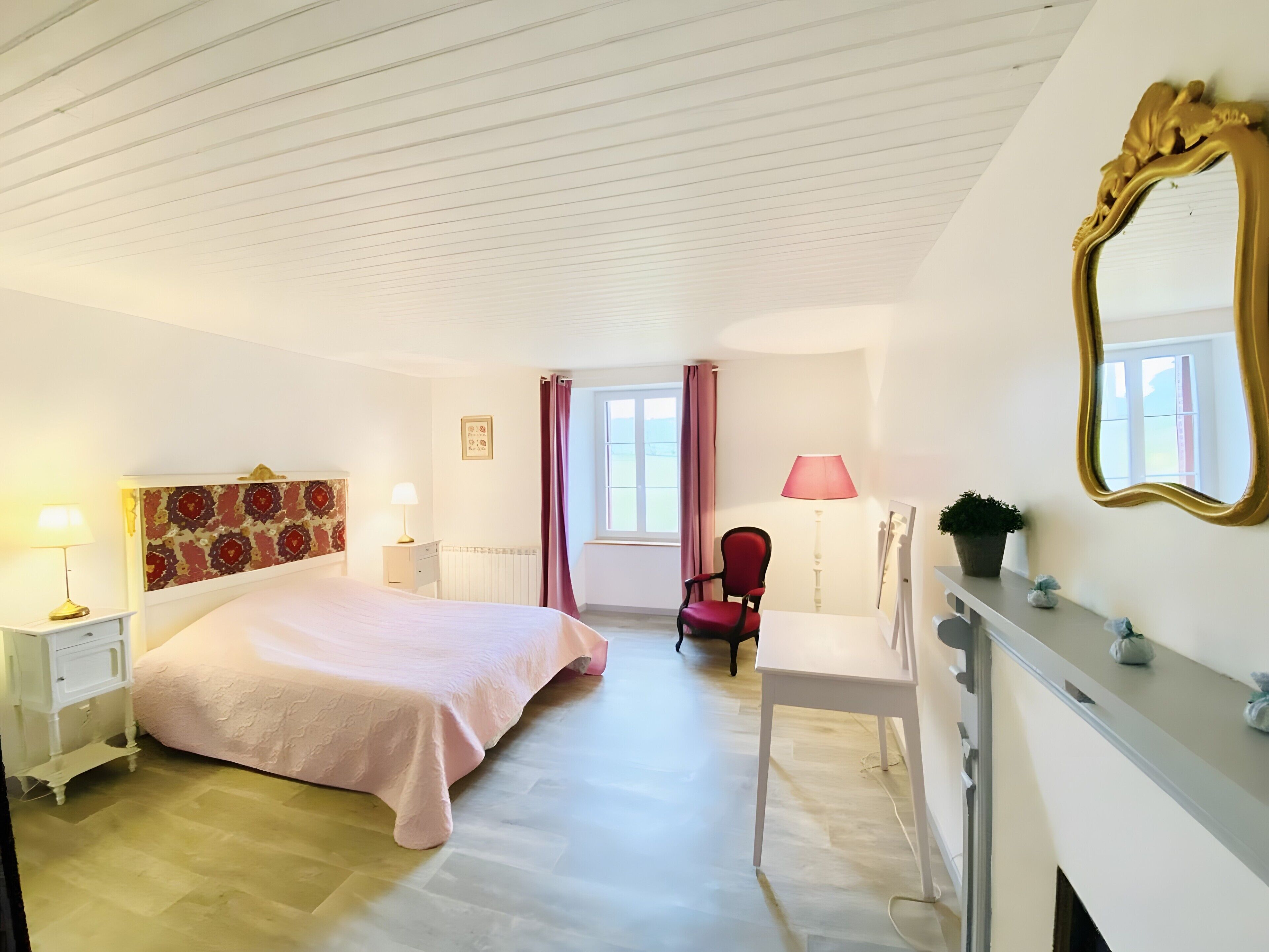 Un dormitorio con cama, una silla, un escritorio, un espejo y una ventana con cortinas.