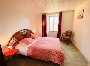 Quarto com cama, cadeira, mesa de cabeceira e janela com cortinas.
