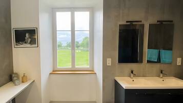 Un baño con ventana, lavamanos, espejo y una foto enmarcada en la pared.