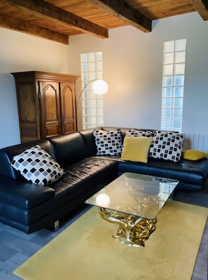 Uma sala de estar moderna com um sofá de couro preto, almofadas estampadas, uma mesa de centro de vidro e um armário de madeira.