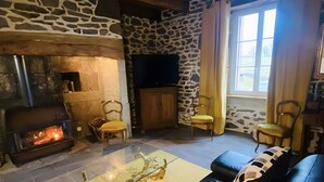 Una habitación con paredes de piedra, chimenea, televisor y dos sillones amarillos.