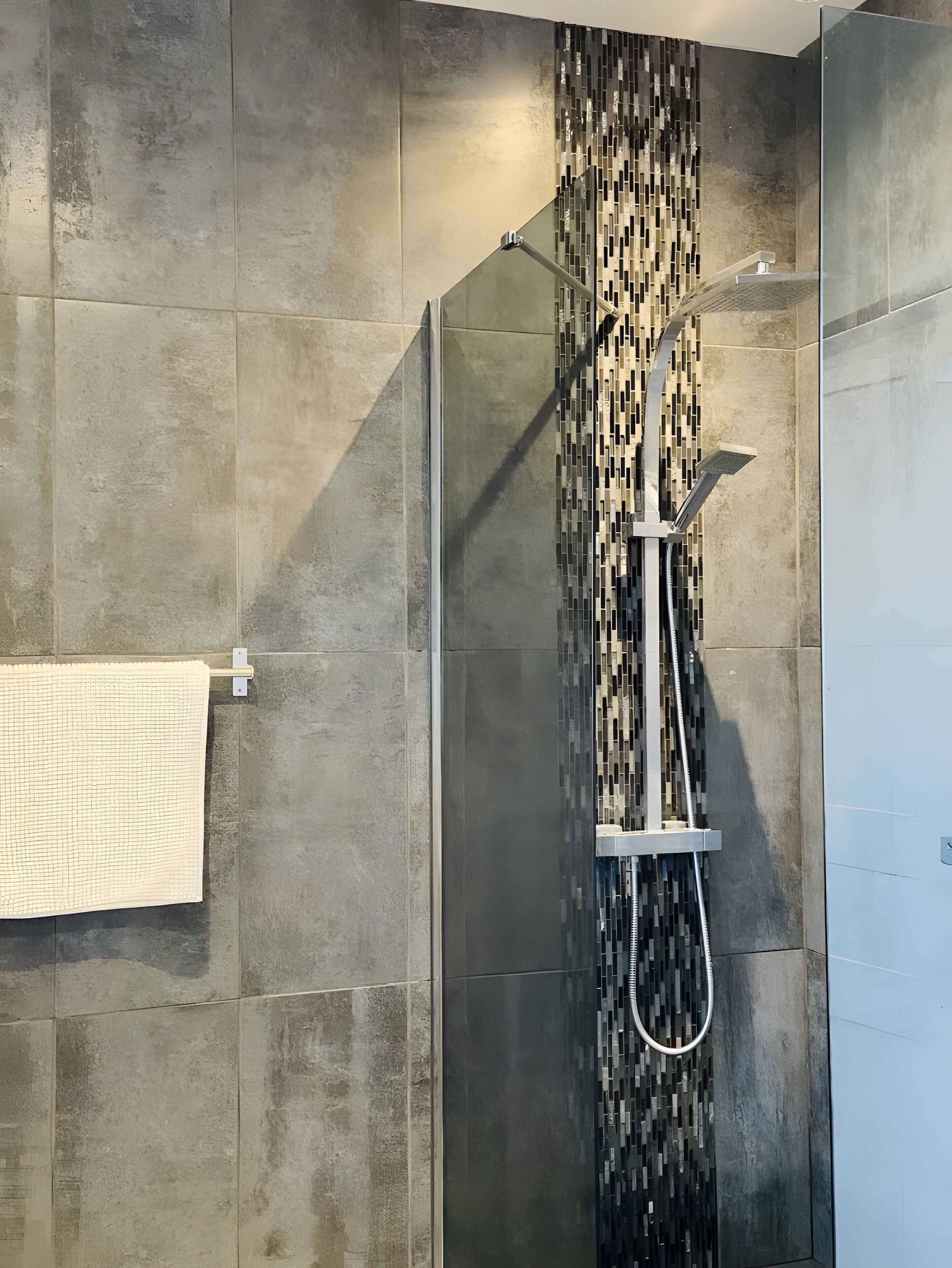 Een douche met een glazen deur, een betegelde wand en een handdoek aan een rek.