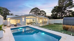 Una casa moderna con piscina, un espacio exterior cubierto y un césped bien cuidado.