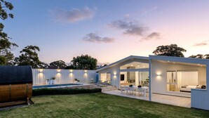 Una casa moderna con piscina, mobiliario exterior y un amplio ventanal que da al interior.