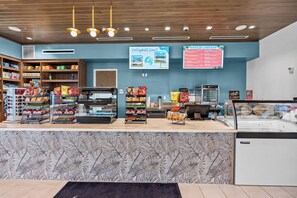 Eine Snackbar mit Regalen voller Chips und Snacks, einer Kühlvitrine und einer Tafel, die den 'Breeze Canteen' und den 'Volleyball Court' bewirbt.
