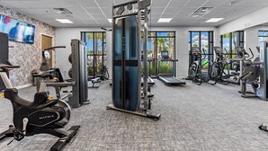 A modern gym with cardio machines, weight training equipment, and large windows offering views of palm trees. - 5BR townhouse at Windsor Cay Resort (Clermont)